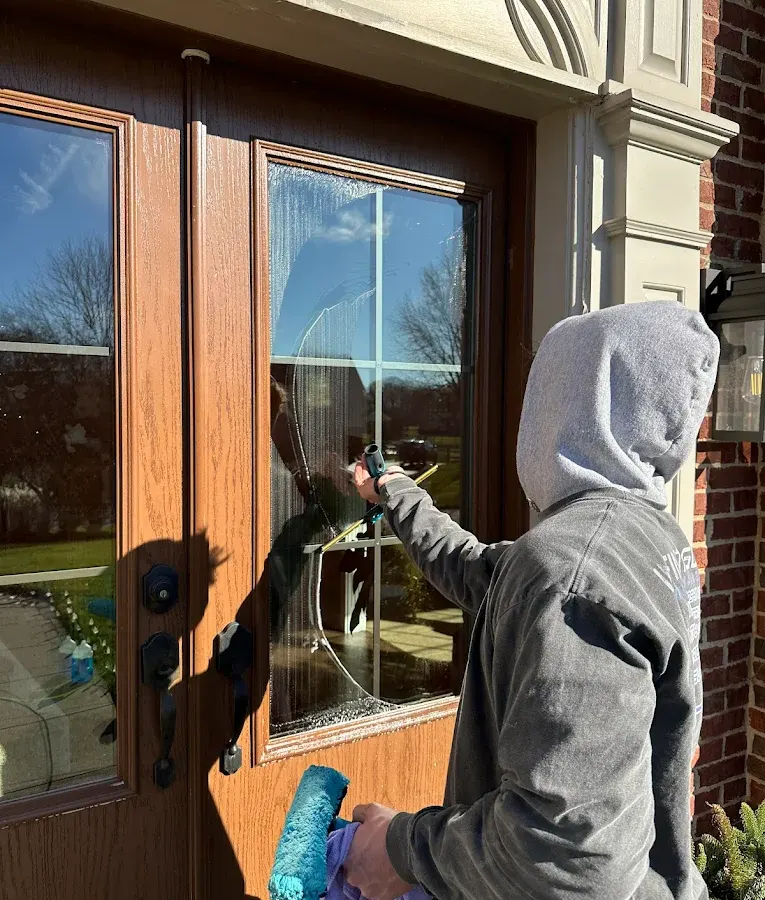 Technician cleaning the glass of a wooden front door with a squeegee