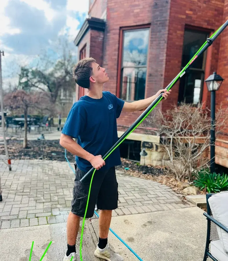Technician cleaning second-story windows of a brick building with a water-fed pole
