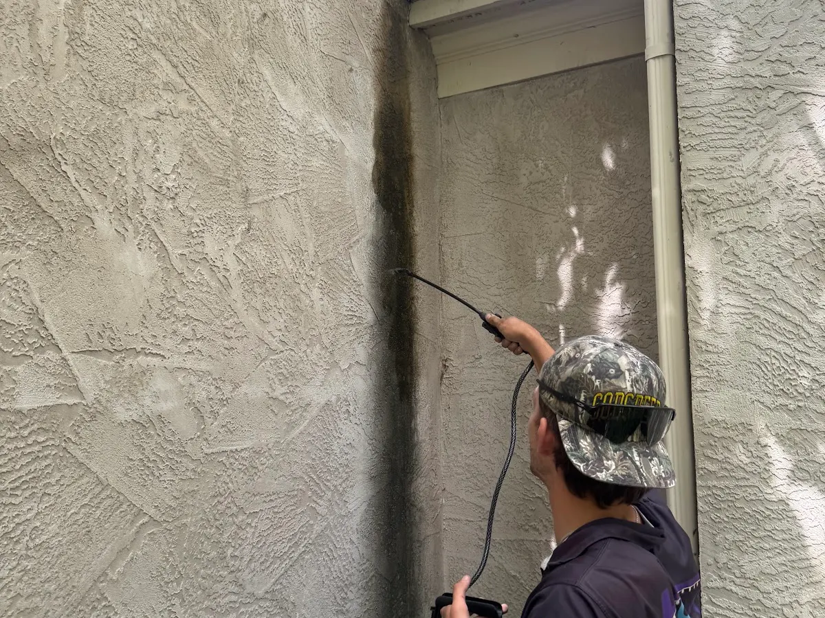 Technician soft washing a stucco wall