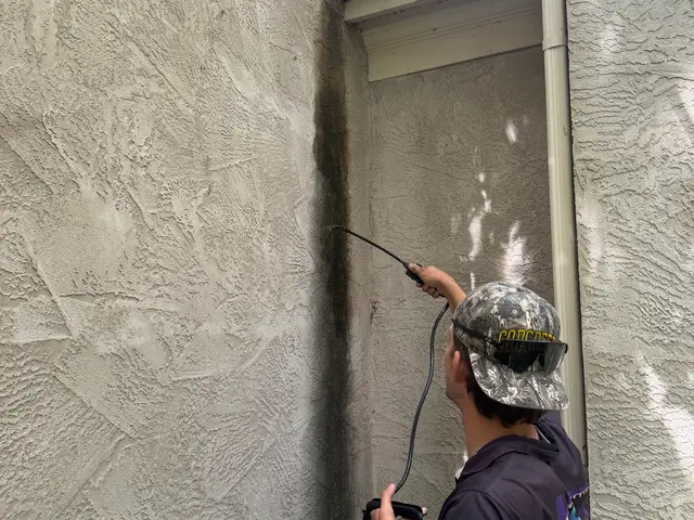 Technician soft washing a stucco wall