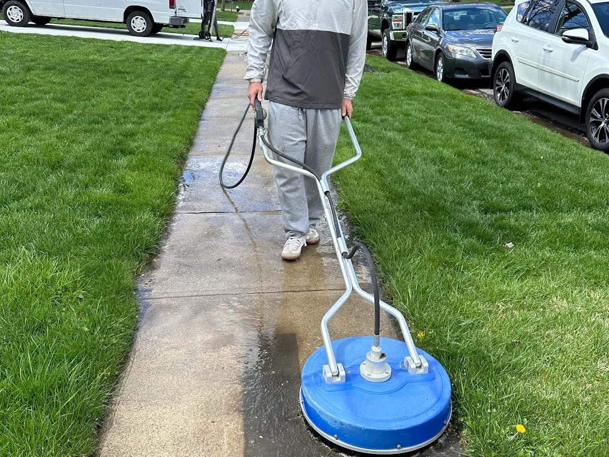 Technician pressure washing a concrete walkway with a surface cleaner