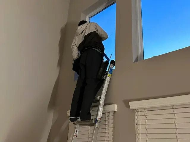 Technician on a ladder cleaning a tall interior window
