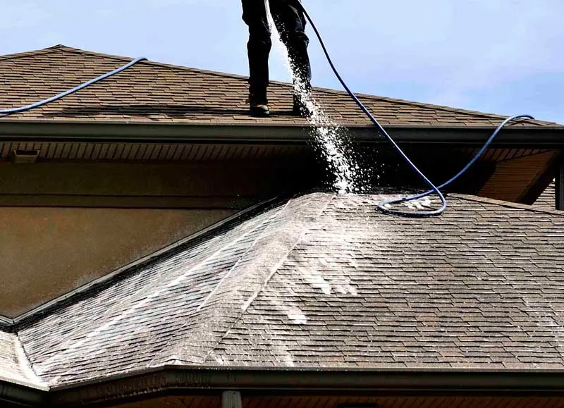 Soft-wash solution being applied to an asphalt shingle roof from the ridge